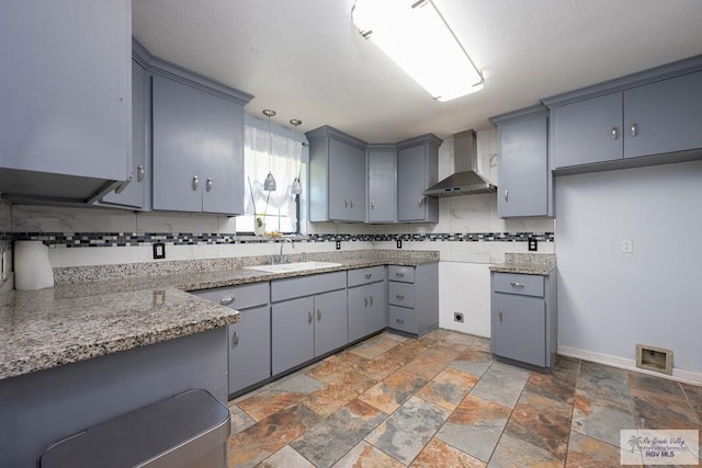 5906 Sunrise Blvd, Harlingen, TX 78552 - kitchen featuring wall chimney range hood, a sink, gray cabinets, stone tile floors, and backsplash