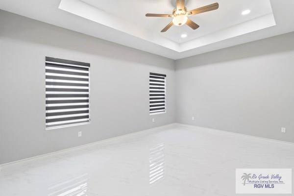 empty room with ceiling fan and a tray ceiling