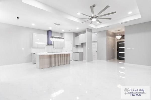 kitchen featuring white cabinetry, a kitchen island, hanging light fixtures, and wall chimney range hood