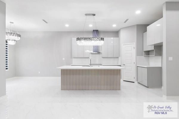 kitchen featuring pendant lighting, a center island with sink, and white cabinetry