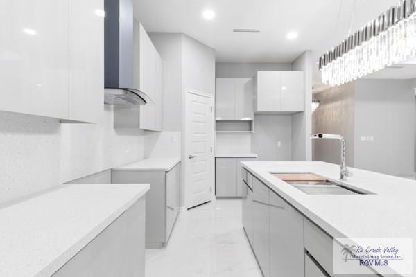 kitchen featuring white cabinetry, wall chimney range hood, and sink