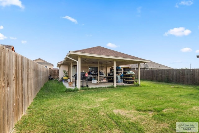 back of house featuring a yard, a shingled roof, a patio, and a fenced backyard