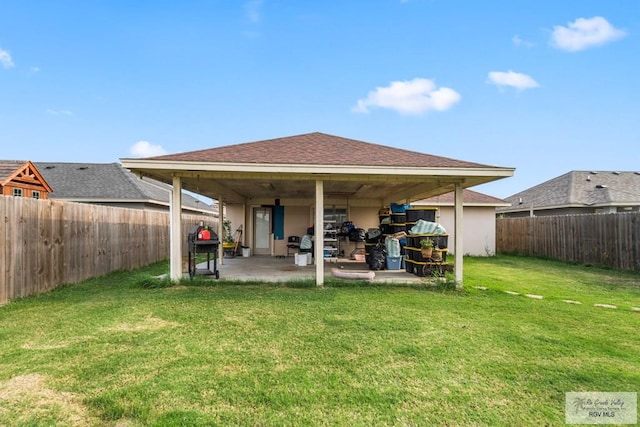 rear view of house featuring a fenced backyard, roof with shingles, a lawn, stucco siding, and a patio area