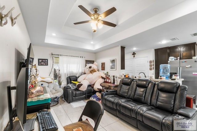 living room featuring light tile patterned floors, visible vents, a raised ceiling, and a ceiling fan