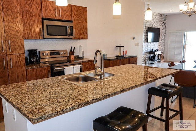 kitchen with decorative light fixtures, tasteful backsplash, an island with sink, sink, and stainless steel appliances