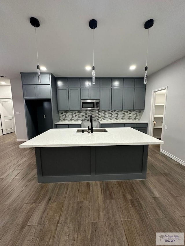 2299 Athens St, Brownsville, TX 78520 - kitchen with stainless steel microwave, backsplash, gray cabinets, dark wood-style flooring, and an island with sink