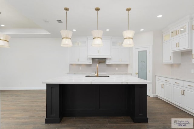 kitchen with a center island with sink, light stone counters, white cabinetry, and dark wood-type flooring