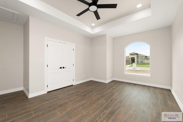 empty room with ceiling fan, dark hardwood / wood-style flooring, and a tray ceiling