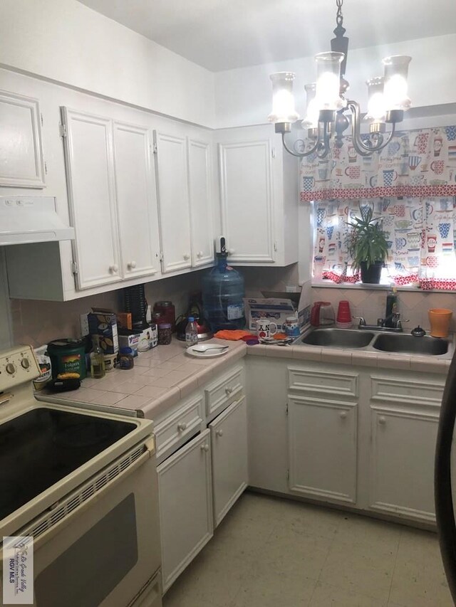 kitchen featuring white cabinetry, tile counters, ventilation hood, white range with electric cooktop, and a chandelier