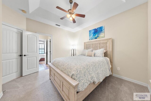 carpeted bedroom with ceiling fan and a raised ceiling