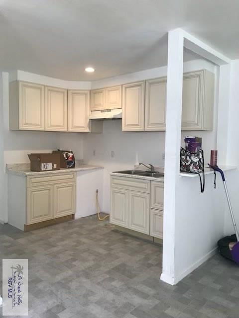 kitchen with cream cabinets, recessed lighting, under cabinet range hood, a sink, and light countertops