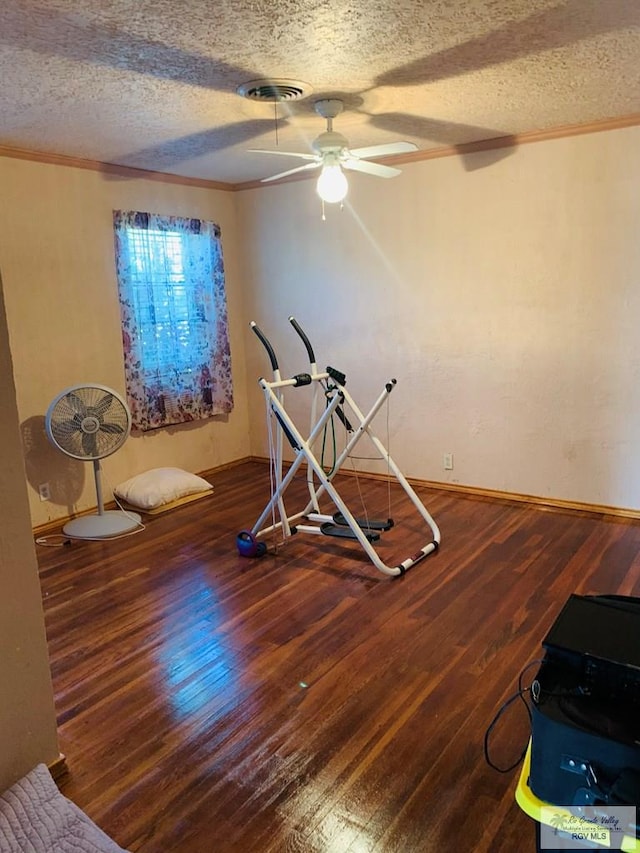 interior space with a textured ceiling, ceiling fan, ornamental molding, and dark wood-type flooring