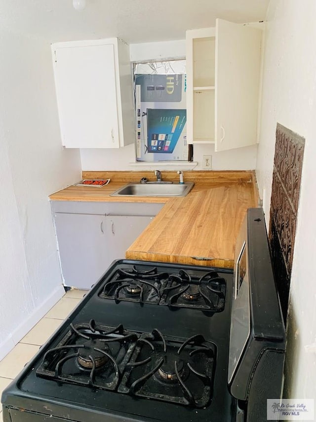 kitchen with sink, light tile patterned floors, wooden counters, black gas stove, and white cabinets