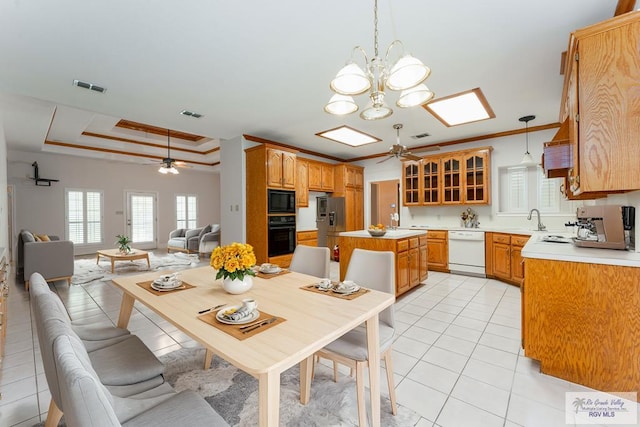 tiled dining area with a tray ceiling, sink, ceiling fan with notable chandelier, and ornamental molding