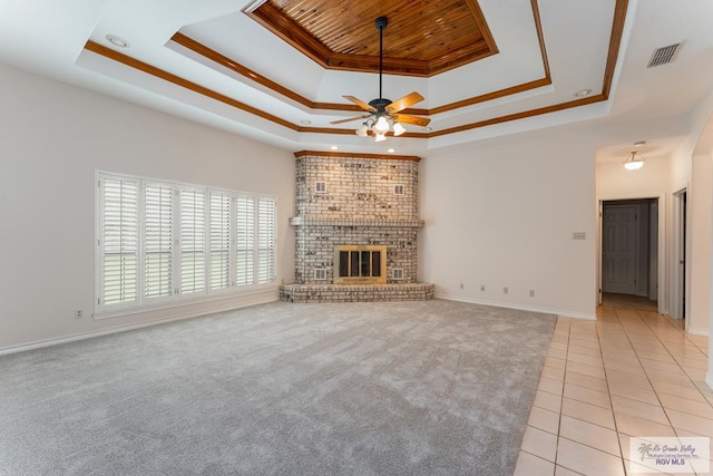 unfurnished living room featuring a raised ceiling, ceiling fan, and a brick fireplace