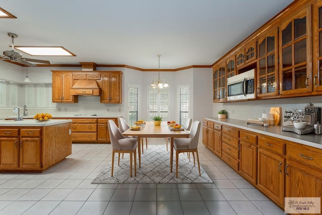 kitchen with ceiling fan with notable chandelier, crown molding, hanging light fixtures, light tile patterned floors, and custom range hood