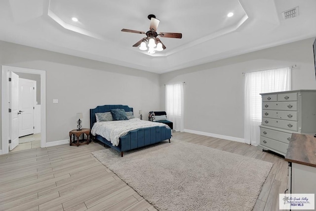 bedroom with light hardwood / wood-style flooring, ceiling fan, and a tray ceiling