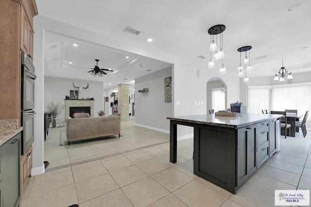 kitchen with double oven, decorative light fixtures, dark stone countertops, a center island, and ceiling fan