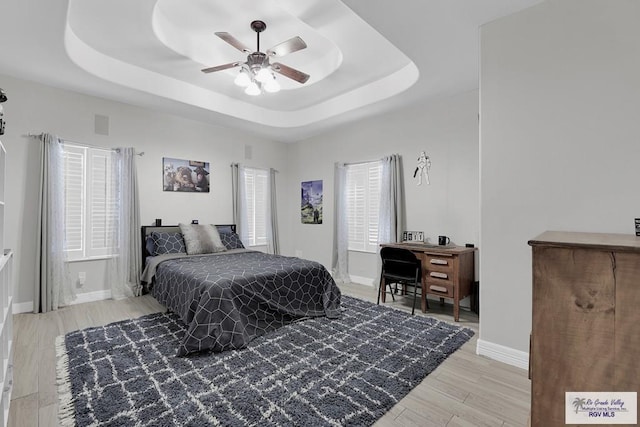 bedroom with light hardwood / wood-style flooring, ceiling fan, and a tray ceiling