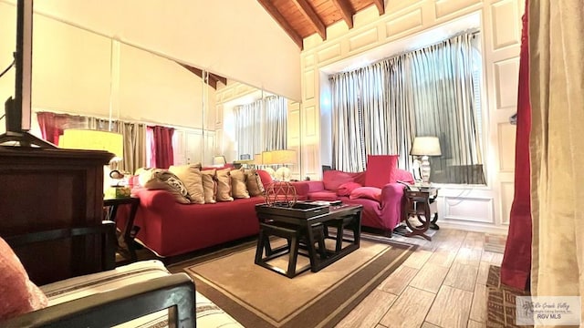 living area featuring beamed ceiling, wood finished floors, a decorative wall, wooden ceiling, and high vaulted ceiling