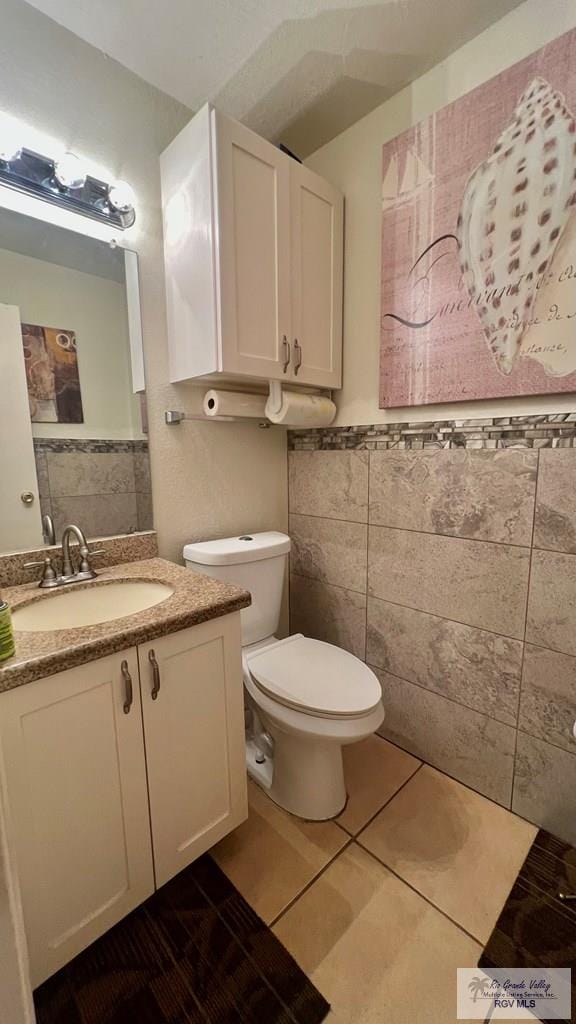 half bath featuring a wainscoted wall, tile patterned floors, toilet, vanity, and tile walls