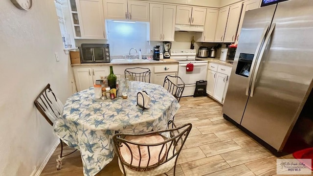 kitchen with a sink, electric range, white cabinetry, stainless steel fridge with ice dispenser, and light countertops