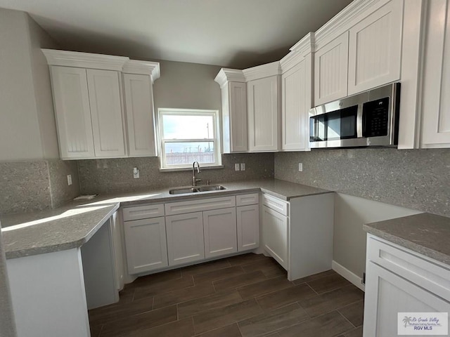 kitchen featuring stainless steel microwave, wood finish floors, decorative backsplash, white cabinets, and a sink