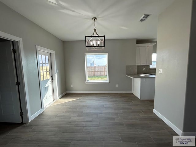unfurnished dining area featuring visible vents, baseboards, an inviting chandelier, and dark wood-style flooring