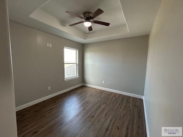 unfurnished room featuring a tray ceiling, baseboards, and dark wood-type flooring