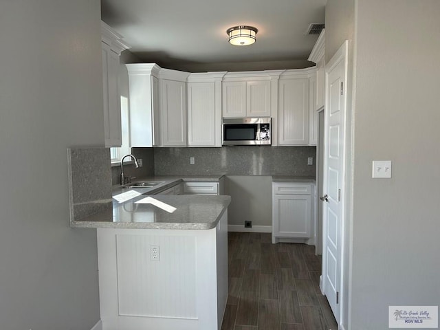 kitchen featuring a sink, stainless steel microwave, backsplash, white cabinetry, and a peninsula