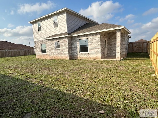 back of property featuring brick siding, a yard, a shingled roof, and a fenced backyard