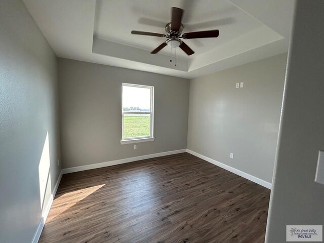 spare room with a tray ceiling, baseboards, dark wood-style flooring, and ceiling fan