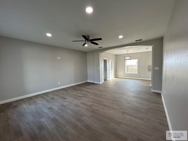 unfurnished room with dark wood-type flooring, baseboards, arched walkways, and ceiling fan