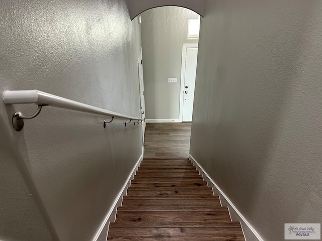 stairway with baseboards, arched walkways, wood finished floors, and a textured wall