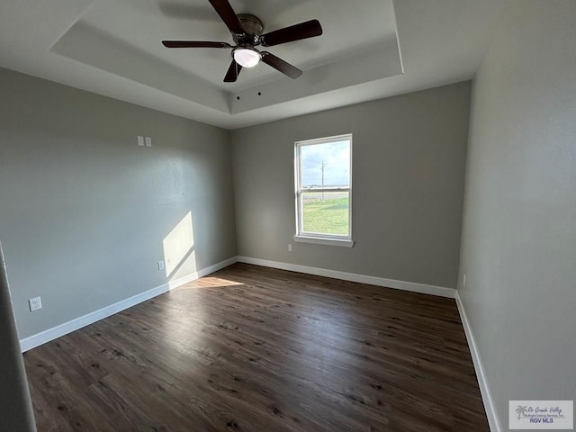 spare room featuring baseboards, a raised ceiling, dark wood-type flooring, and a ceiling fan