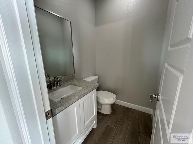 bathroom with wood finish floors, baseboards, toilet, and vanity