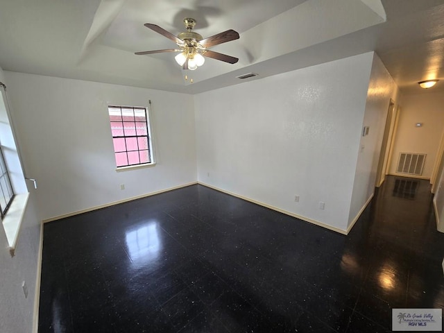 empty room with ceiling fan and a raised ceiling