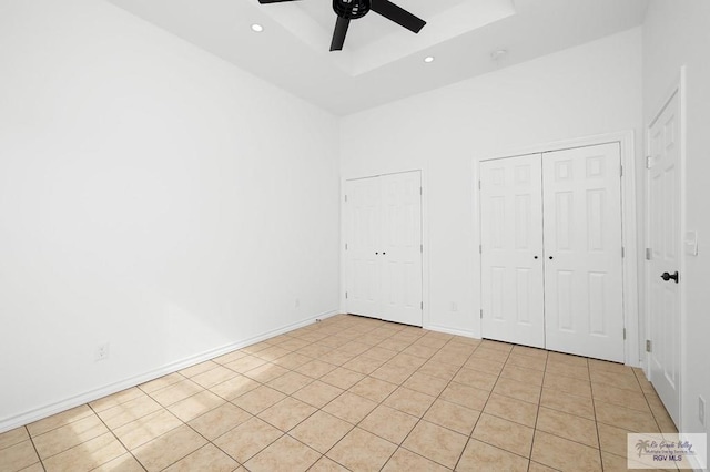 unfurnished bedroom with light tile patterned floors, two closets, and ceiling fan