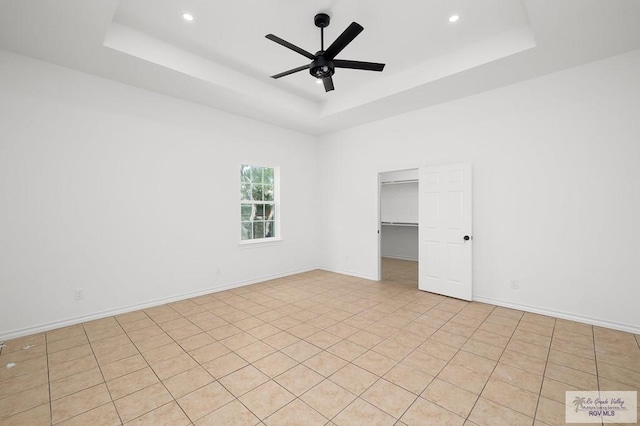 tiled empty room featuring a raised ceiling and ceiling fan