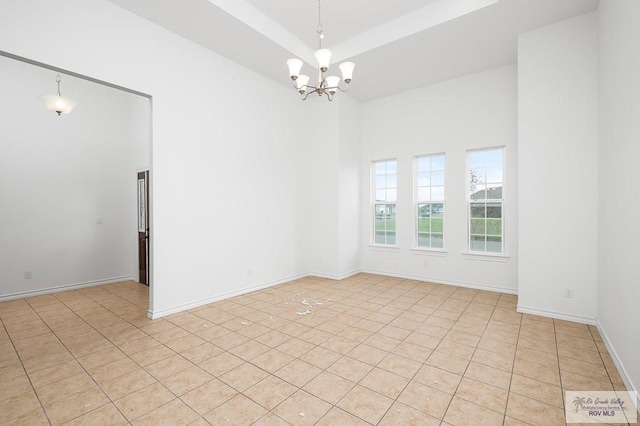 unfurnished room with a towering ceiling, a tray ceiling, an inviting chandelier, and light tile patterned flooring