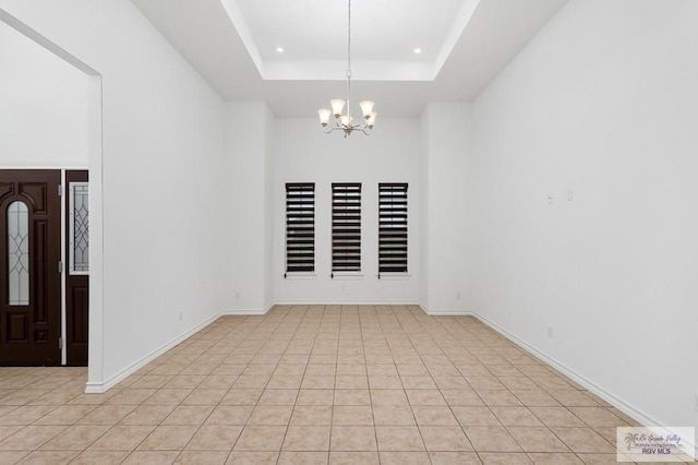 unfurnished room featuring a raised ceiling, light tile patterned flooring, and a chandelier