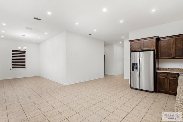 kitchen featuring stainless steel fridge, light stone countertops, dark brown cabinetry, and a chandelier