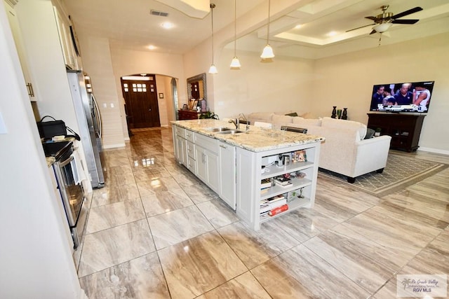 kitchen with pendant lighting, white cabinets, a kitchen island with sink, stainless steel appliances, and light stone countertops