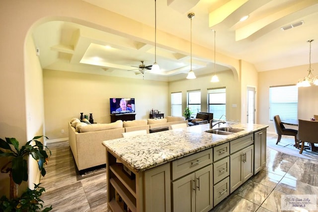 kitchen with sink, ceiling fan with notable chandelier, light stone countertops, a center island with sink, and decorative light fixtures