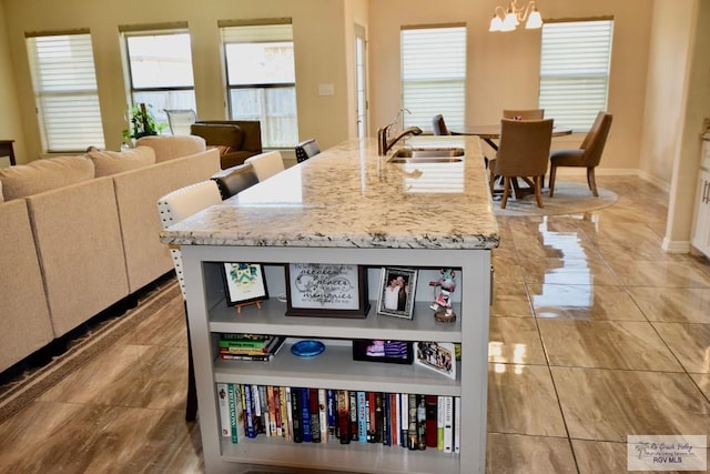 kitchen featuring light stone counters, an island with sink, decorative light fixtures, and sink