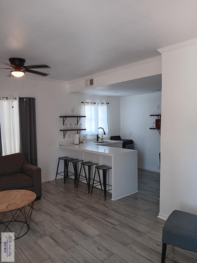 kitchen with ceiling fan, kitchen peninsula, light wood-type flooring, a kitchen bar, and ornamental molding