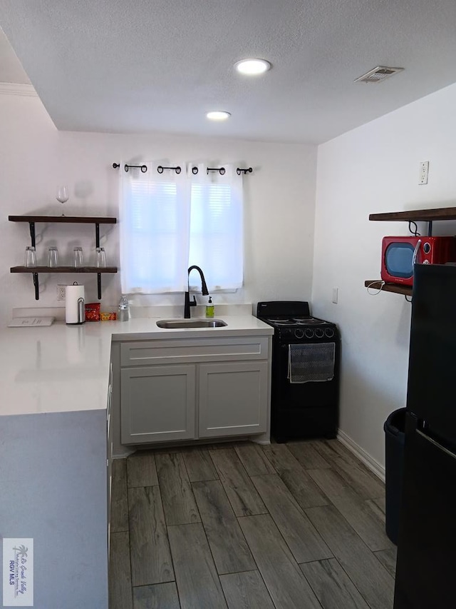 126 E Esperanza St Unit 101, South Padre Island, TX 78597 - kitchen featuring black appliances, wood finished floors, light countertops, open shelves, and a textured ceiling
