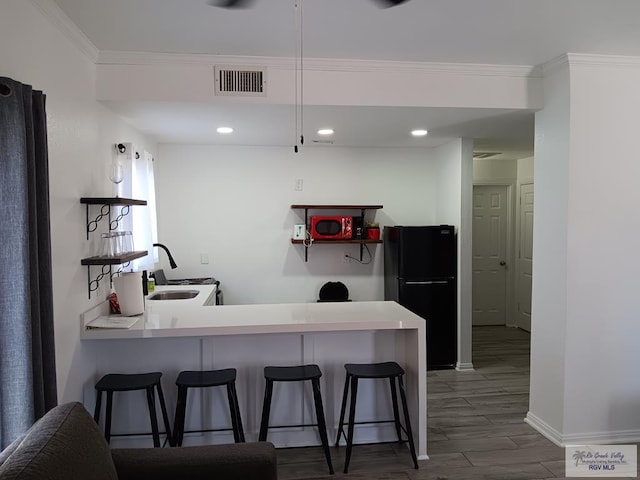 kitchen with a breakfast bar, sink, dark wood-type flooring, kitchen peninsula, and black refrigerator