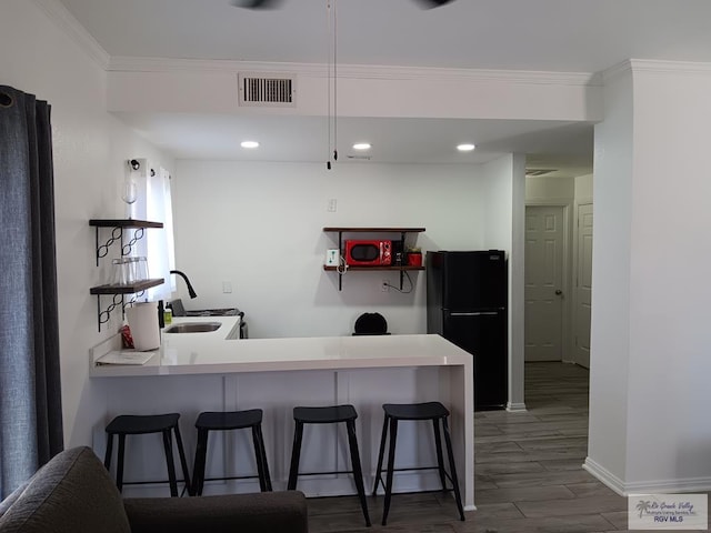 126 E Esperanza St Unit 101, South Padre Island, TX 78597 - kitchen featuring freestanding refrigerator, a breakfast bar area, a peninsula, light countertops, and dark wood-style flooring