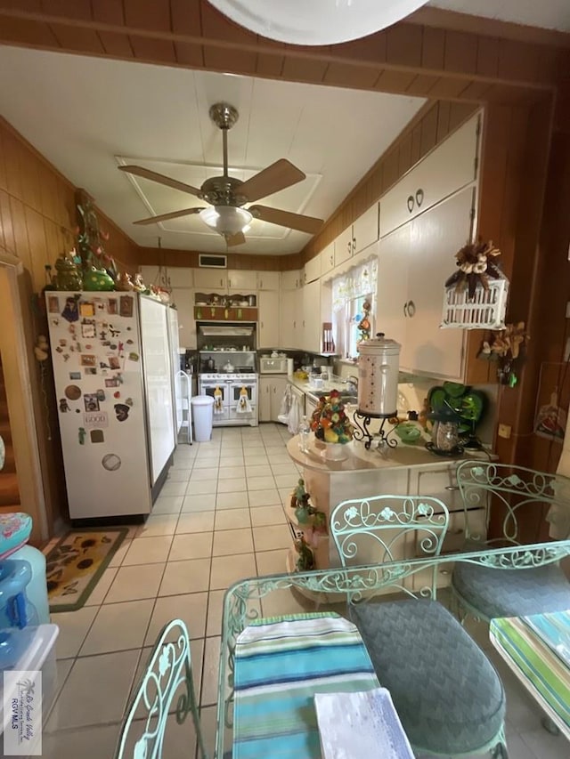 kitchen with ceiling fan, light tile patterned flooring, white appliances, wooden walls, and white cabinets